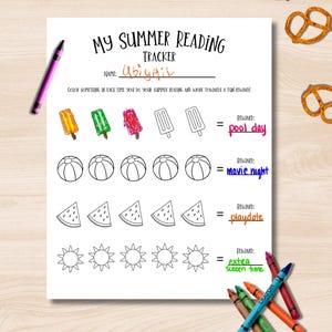 May include: A white summer reading tracker with the title "MY SUMMER READING TRACKER" and the name "Abigail" written on it. The tracker includes illustrations of popsicles, beach balls, watermelon slices, and suns. Crayons and pretzels are also visible.