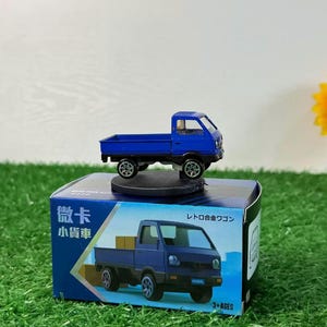 May include: A blue toy truck with a white bed and black wheels. The truck is on a display stand with a blue and white box. The box has Japanese text that says "truck" and "toy".