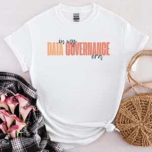 Puede incluir: Camiseta blanca con el texto "in my DATA GOVERNANCE era" impreso en naranja y azul.
