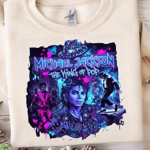 May include: Cream-colored sweatshirt featuring a vibrant graphic of Michael Jackson. The design includes the text "Michael Jackson The King of Pop" in a neon-style font, along with images of Jackson in various poses, and a fedora hat.