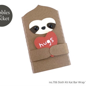 May include: A brown sloth holding a red heart that says "hugs" on it. The sloth is holding the heart in front of its chest. The sloth is made of paper and is part of a kit to make a Kit Kat bar wrapper.