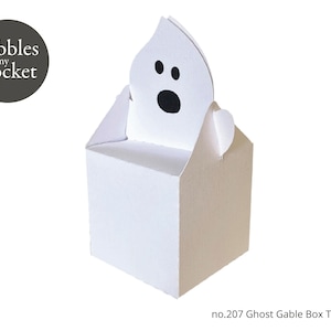 Könnte beinhalten: Eine weiße Giebelbox mit einem geisterförmigen Ausschnitt oben. Der Geist hat schwarze Augen und einen Mund. Die Box ist mit "pebbles in my pocket" und "no.207 Ghost Gable Box Template" beschriftet.