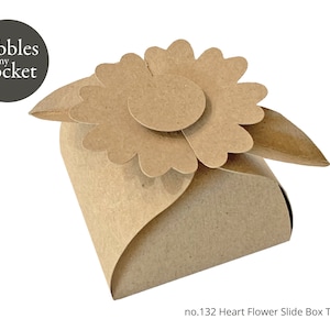 Puede incluir: Una caja artesanal de papel marrón con una tapa en forma de flor. La caja es un diseño de caja deslizante, con el texto "pebbles in my pocket" en un círculo en la parte superior izquierda. El texto "no.132 Heart Flower Slide Box Template" está en la parte inferior.