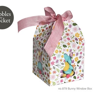 Puede incluir: Una caja blanca con un patrón floral y una cinta rosa. La caja tiene una ventana en forma de conejo y está llena de caramelos de colores. La caja está etiquetada "no. 879 Bunny Window Box Template".