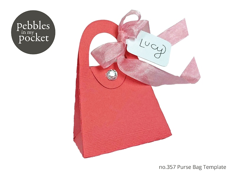 May include: A red purse-shaped gift box with a pink ribbon and a white tag that says "Lucy". The box is decorated with a rhinestone.