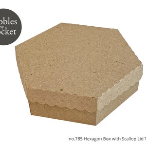 Puede incluir: Una caja hexagonal marrón con una tapa festoneada. La caja está hecha de cartón y tiene una superficie texturizada. El texto "no.785 Hexagon Box with Scallop Lid Template" está impreso en la parte inferior de la imagen.