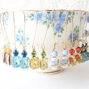 May include: Eight pairs of gold dangle earrings with various colored glass and porcelain beads. The earrings are displayed on a white teacup with floral designs.