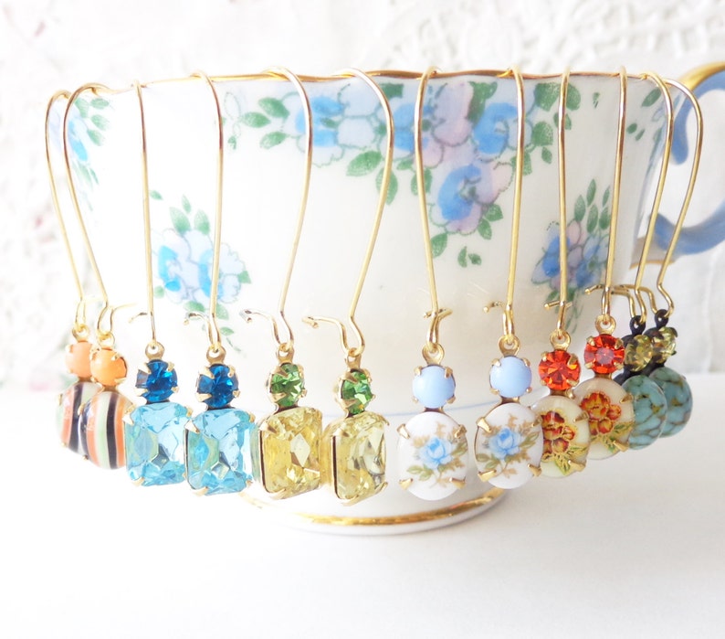 May include: Eight pairs of gold dangle earrings with various colored glass and porcelain beads. The earrings are displayed on a white teacup with floral designs.