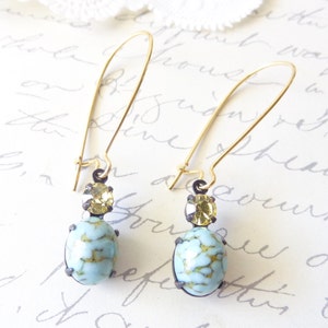 May include: A pair of gold dangle earrings with a light blue and gold stone. The earrings have a simple design and are perfect for everyday wear.
