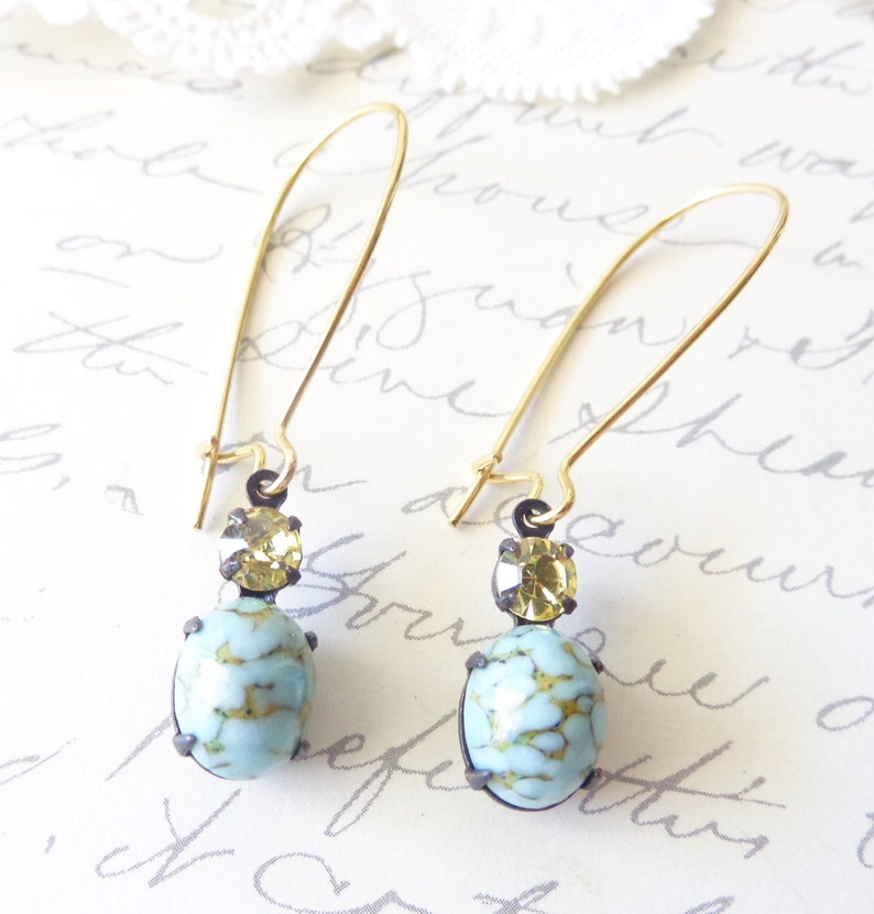 May include: A pair of gold dangle earrings with a light blue and gold stone. The earrings have a simple design and are perfect for everyday wear.