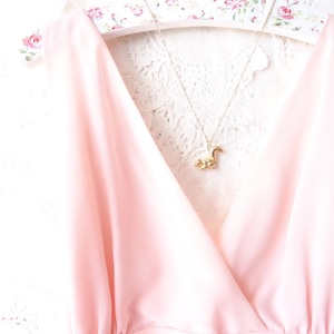 Puede incluir: Una blusa rosa sin mangas con escote en V y un collar con un colgante de ardilla dorado.