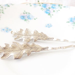 Puede incluir: Dos pinzas para el pelo de hoja de roble plateadas. Las hojas son texturizadas y tienen un diseño ligeramente en relieve. Las pinzas son simples y elegantes.