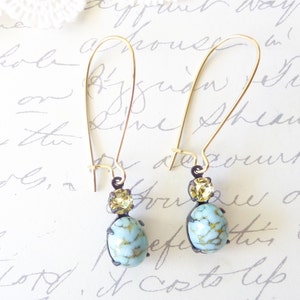 May include: A pair of gold dangle earrings with a light blue and gold oval-shaped stone and a smaller gold stone above it.