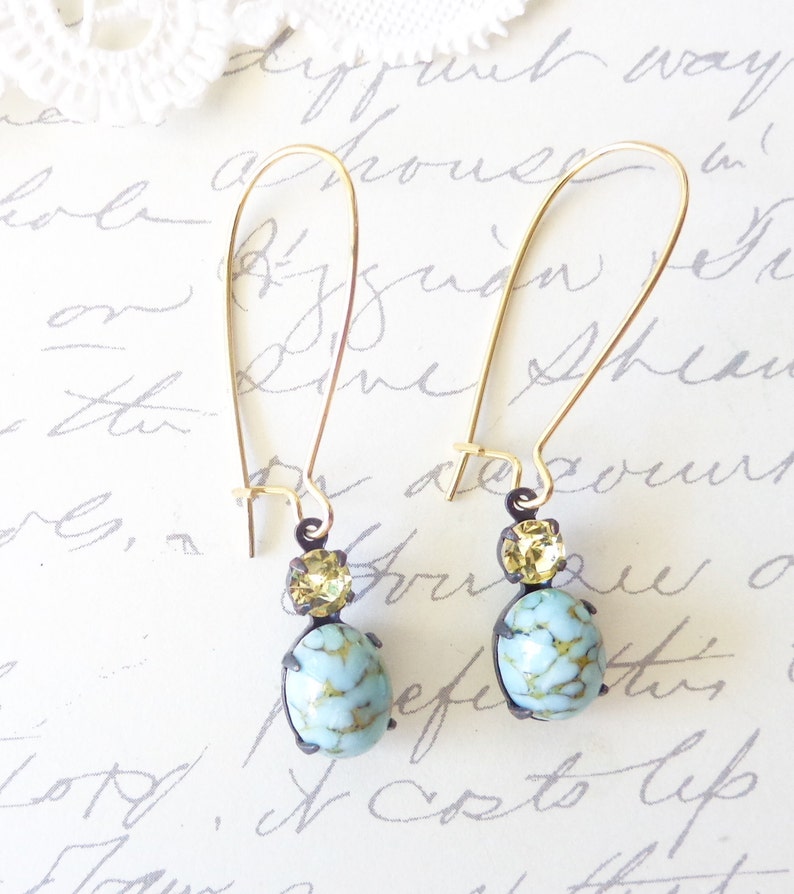 May include: A pair of gold dangle earrings with a light blue and gold oval-shaped stone and a smaller gold stone above it.