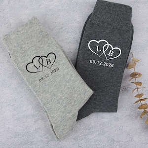 May include: Two pairs of socks, one light grey and one dark grey, are shown. Each sock has a design of two intertwined hearts with the initials "L" and "B" and the date "09.12.2026" printed below. These socks are likely for a wedding or anniversary.