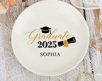 Puede incluir: Plato de anillo de cerámica blanca con un diseño negro y dorado que dice "Graduate 2025" y "Sophia".