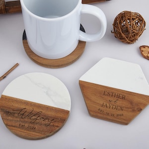 May include: Two wooden coasters with a white marble top. One coaster has the text "The Wilfong Est. 2024" and the other has the text "Esther and Jayden Est. 10.22.2025".