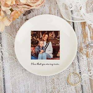 May include: A white ceramic plate with a printed photograph of a mother and child. The plate has the text "I love that you are my mom." The plate is surrounded by flowers and lace.