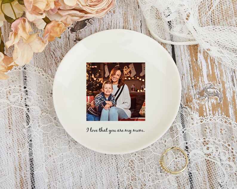 May include: A white ceramic plate with a printed photograph of a mother and child. The plate has the text "I love that you are my mom." The plate is surrounded by flowers and lace.