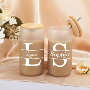 Pode incluir: Dois copos de vidro fosco com tampas de bambu e canudos. Os copos est&atilde;o cheios de um l&iacute;quido castanho e t&ecirc;m os nomes "Layla" e "Sophia" impressos neles.