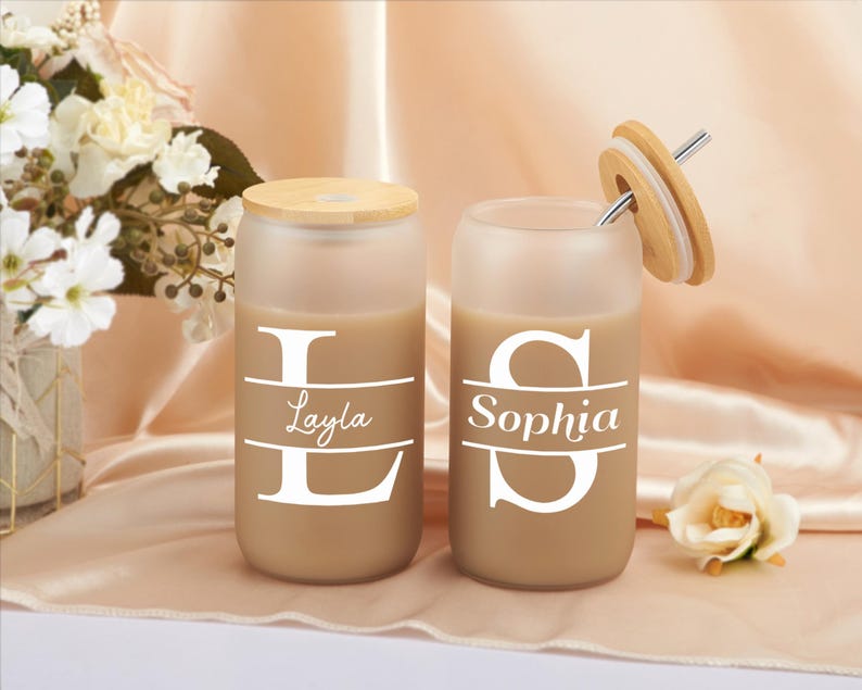 Pode incluir: Dois copos de vidro fosco com tampas de bambu e canudos. Os copos est&atilde;o cheios de um l&iacute;quido castanho e t&ecirc;m os nomes "Layla" e "Sophia" impressos neles.