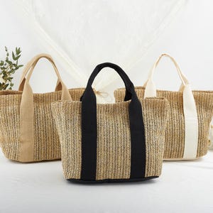 May include: Three straw tote bags with different colored handles. The bag on the left has brown handles, the middle bag has black handles, and the bag on the right has white handles.