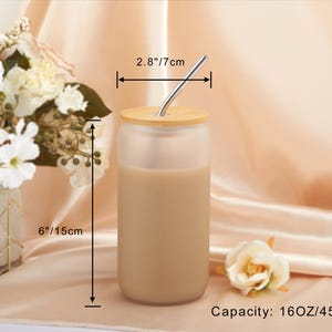 Pode incluir: Um copo de vidro fosco com tampa de madeira e um canudo de a&ccedil;o inoxid&aacute;vel. O copo est&aacute; cheio de um l&iacute;quido castanho claro e mede 15 cm de altura e 7 cm de largura. Capacidade: 450 ml.