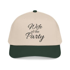May include: A beige baseball cap with a dark green brim and a dark green button on top. The front of the cap features the black embroidered text "Wife of the Party" in a cursive script font. The cap has a structured crown and a curved visor.