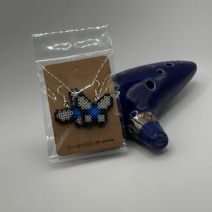 Könnte beinhalten: Ein Paar handgefertigte Schmetterlings-Ohrringe aus blauen, weißen und schwarzen Perlen. Die Ohrringe sind auf einer braunen Karte mit dem Text "Handmade with love" verpackt.