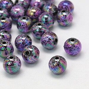 May include: A collection of iridescent purple beads with a white swirl design. The beads are round and have a hole in the center for stringing.