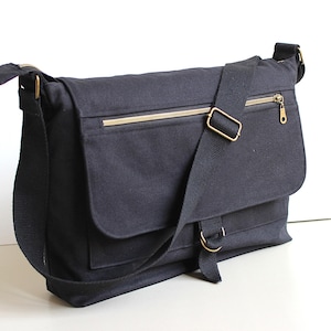 Könnte beinhalten: Marineblaue Messenger-Tasche mit Klappenverschluss und verstellbarem Schultergurt. Die Tasche hat einen goldfarbenen Reißverschluss und Beschläge. Die Tasche ist aus strapazierfähigem Canvas-Material.