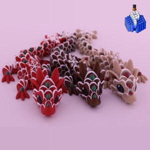 May include: Three articulated dragon figurines featuring a scale-like texture with snowflake patterns. The dragons are colored in red, dark brown, and light tan, each accented with white outlines and small green or red gems on their heads.