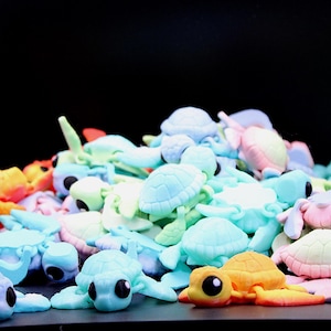 Könnte beinhalten: Eine Ansammlung farbenfroher Schildkrötenfiguren in verschiedenen Pastelltönen, darunter Blau, Grün, Rosa und Gelb. Die Schildkröten haben große, ausdrucksstarke Augen und sind vor einem dunklen Hintergrund angeordnet.