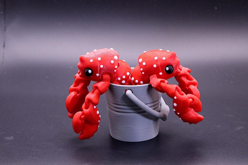 May include: Two red and white spotted toy crabs are holding onto the rim of a gray plastic bucket.
