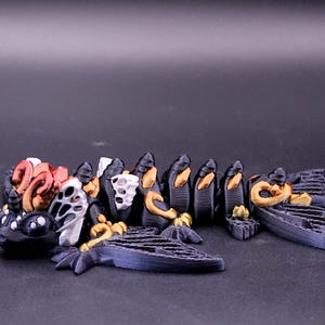 以下が含まれることがあります： 詳細な3Dプリント彫刻。青い骨格構造と複雑なディテールを持つ、様式化された生き物。赤、白、金、黒の要素を取り入れ、有機的な形状と質感が特徴。全体的なデザインは、ファンタジーまたは芸術的なテーマを示唆しています。