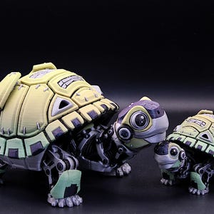 May include: Two robotic turtle figurines, one larger than the other. The larger turtle is yellow and green with black accents, while the smaller turtle is green and black with yellow accents. Both turtles have large, round eyes and detailed, articulated legs.