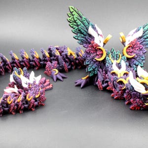 May include: A detailed, articulated dragon figurine in shades of purple, red, gold, white, and green. The dragon has large, feathered wings and a segmented body. The head and body are adorned with intricate details and gold accents.
