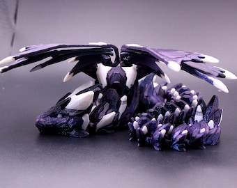 May include: A detailed, 3D-printed dragon figurine in shades of purple, black, and white. The dragon has outstretched wings and a serpentine body, with sharp, white accents on its wings and body. The figurine is set against a dark background.