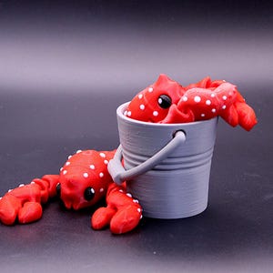 May include: Two red and white polka dot crabs, one in a gray bucket and one lying on the ground.