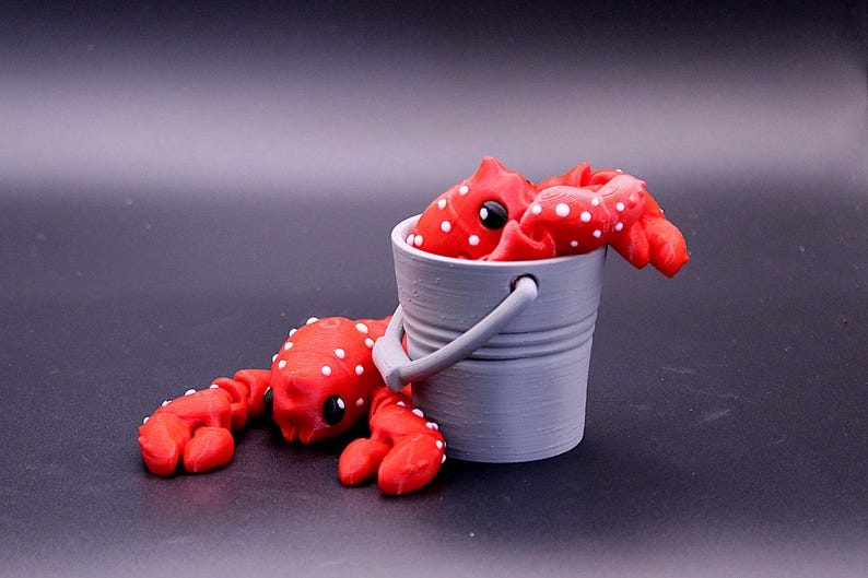 May include: Two red and white polka dot crabs, one in a gray bucket and one lying on the ground.