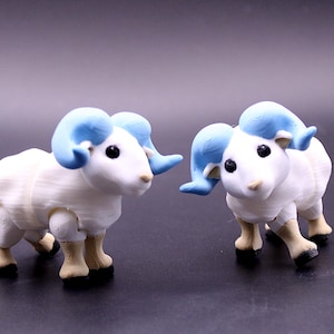 May include: Two small, white ram figurines with light blue horns and black eyes. The rams have tan legs and black hooves. The figurines are standing on a dark surface.