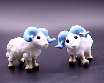 May include: Two small, white ram figurines with light blue horns and black eyes. The rams have tan legs and black hooves. The figurines are standing on a dark surface.