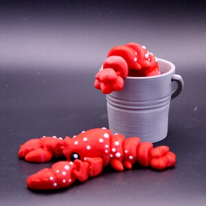 May include: Two red lobster figurines with white spots. One lobster is in a gray metal bucket.