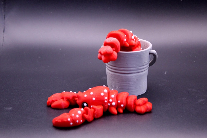 May include: Two red lobster figurines with white spots. One lobster is in a gray metal bucket.