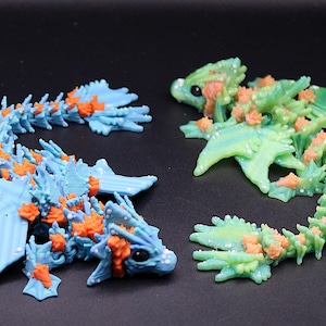 May include: Two small, articulated dragon figurines. One is blue with orange accents, the other is green with orange accents.