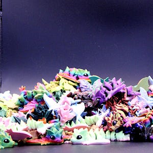 Könnte beinhalten: Ein großer Haufen kleiner, bunter Plastik-Drachenfiguren. Die Drachen sind in verschiedenen Posen und haben unterschiedlich farbige Flügel, Körper und Schwänze.