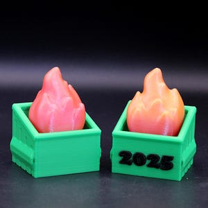 Puede incluir: Dos mini contenedores verdes con llamas naranjas en su interior. El contenedor de la derecha tiene el año 2025 impreso en la parte delantera.