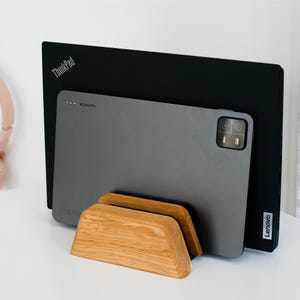 May include: A light-toned wooden stand holding a dark gray Xiaomi tablet and a black Lenovo ThinkPad laptop. The stand features a smooth, angled design with a slot for upright device storage, showcasing the visible brand logos on both electronics.
