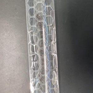 May include: A clear plastic packaging insert with a honeycomb pattern. The insert is designed to hold small items, with multiple hexagonal compartments. The material is transparent, allowing visibility of the contents.