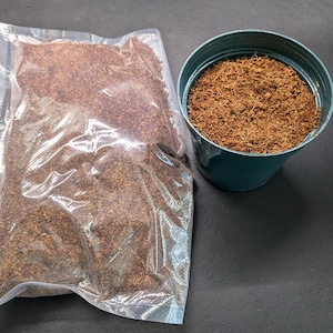 May include: A clear plastic bag filled with brown coconut coir, a type of soil amendment, next to a teal plastic pot filled with the same coir.